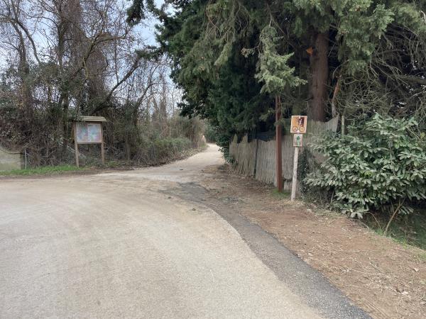 Crossroads between paved road and dirt track. Straw fence on left and map on right side. Road elevated to the path.